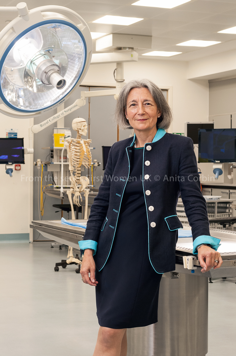 A woman wearing a navy blue dress and matching blazer standing in an operating theatre.