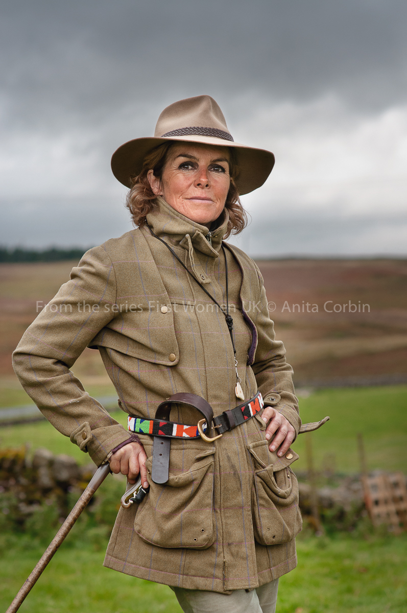 A woman wearing a beige jacket and hat with a multicoloured belt.