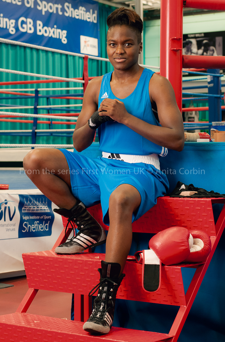 Woman wearing blue wresting gear sitting on red steps leading to a boxing ring.